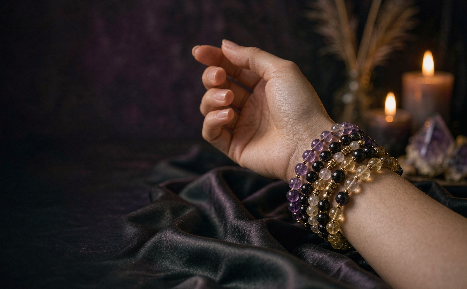 Stacked amethyst, obsidian and citrine crystal bracelets in candlelight