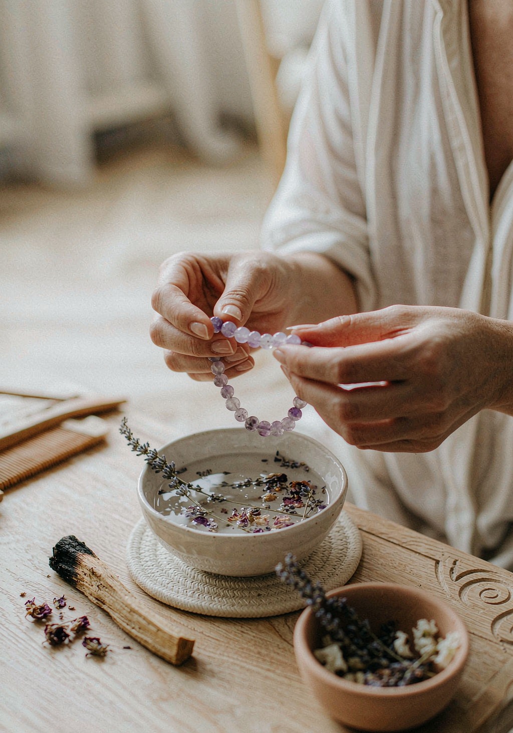 Hands cleansing an amethyst bracelet in a bowl of water and lavender